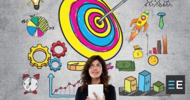 A person holding a tablet standing in front of colorful imagery of targets, gears, rockets, and graphs